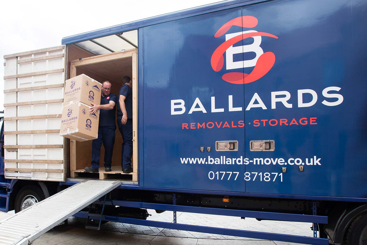 Ballards removals team member carrying 2 cardboard boxes out the side door down the ramp out of a wooden crate in the removals van.