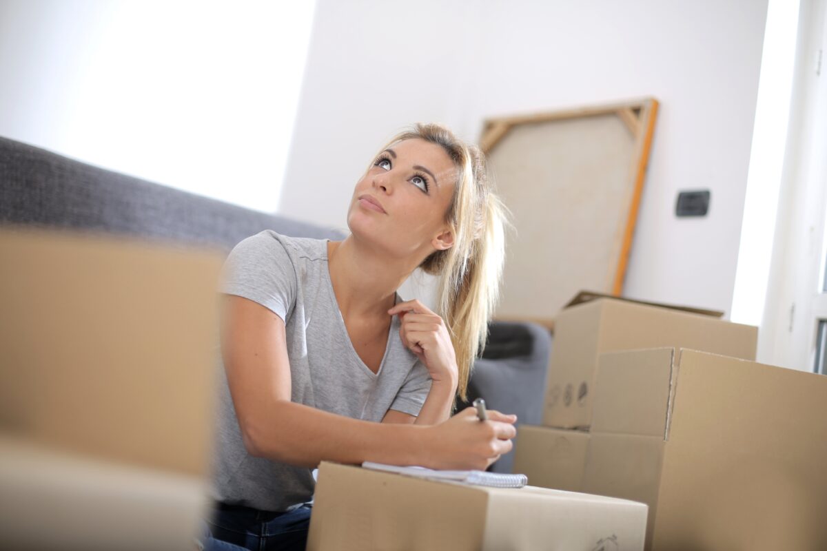 moving day woman writes on notesbookssurrounded by moving boxes