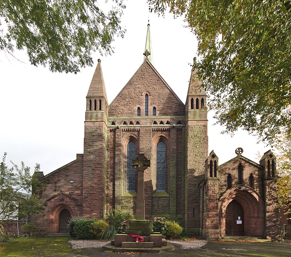 A close‑up view of the west end of St John the Evangelist Church, showing detailed stonework, arched windows, and the textured masonry of the historic building.