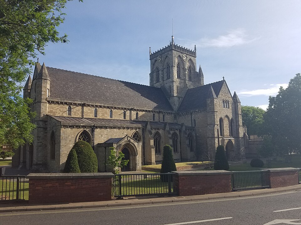A street‑level view of Grimsby Minster from the junction of Bethlehem Street and Church Lane, showing the church’s stone façade, tower and surrounding urban streetscape.
