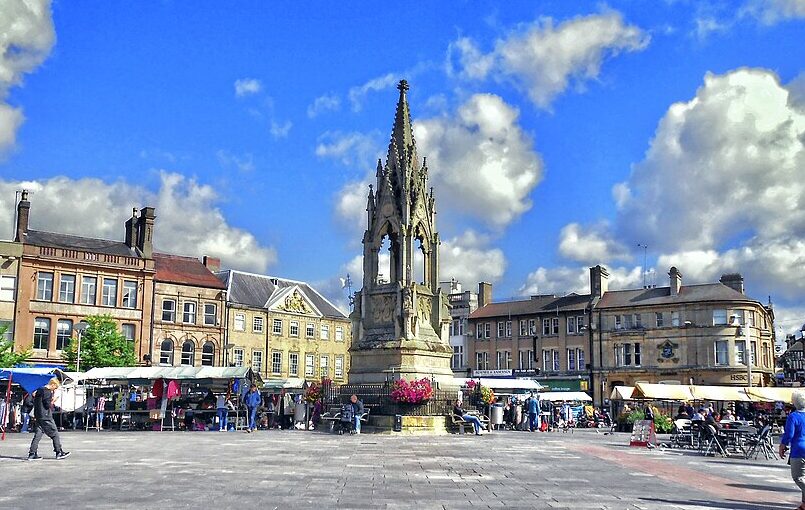 A bright morning scene at Mansfield’s market, showing stalls set up around the Market Place with the Bentinck Memorial standing prominently at the centre.