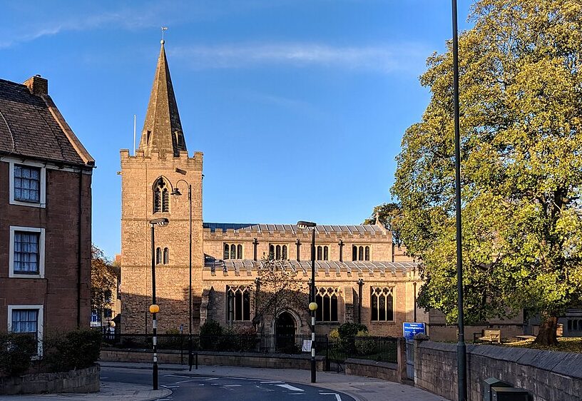 A view of St Peter and St Paul’s Church on Church Street in Mansfield, showing its stone façade, tower and detailed Gothic architecture, with surrounding trees and street elements visible.