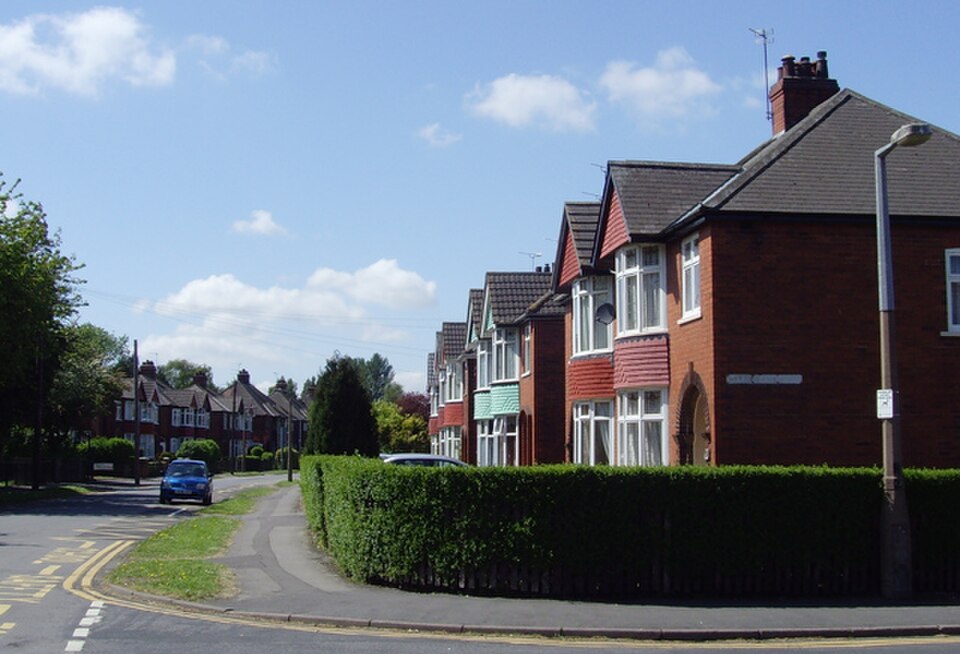 View looking west along Bushfield Road in Scunthorpe from the junction with Maple Tree Way, showing houses, parked cars and the residential streetscape.