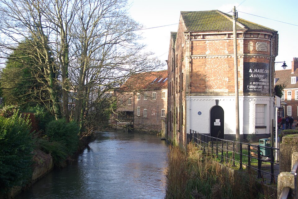 View of the River Bain flowing through Horncastle, with trees, footpaths and surrounding buildings visible along the riverbank.
