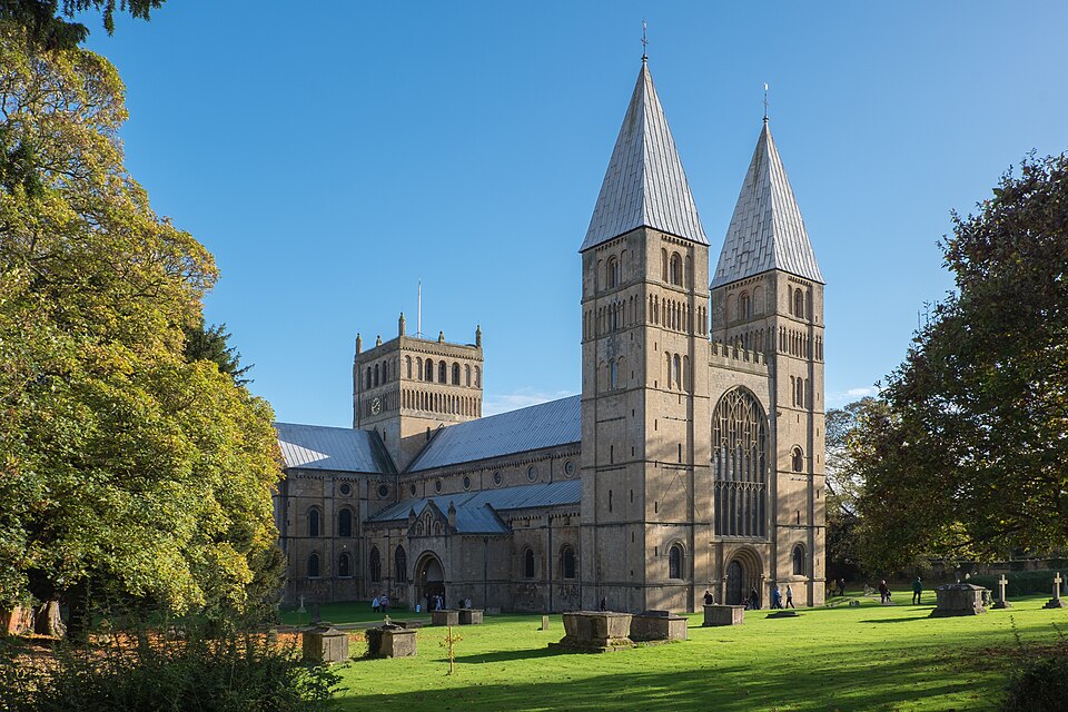 North‑west view of Southwell Minster, showing its twin towers, detailed stonework and surrounding grounds on a clear day.
