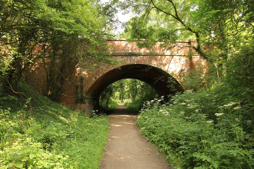 A summer view along the Southwell Trail featuring a large stone bridge surrounded by dense trees and greenery.