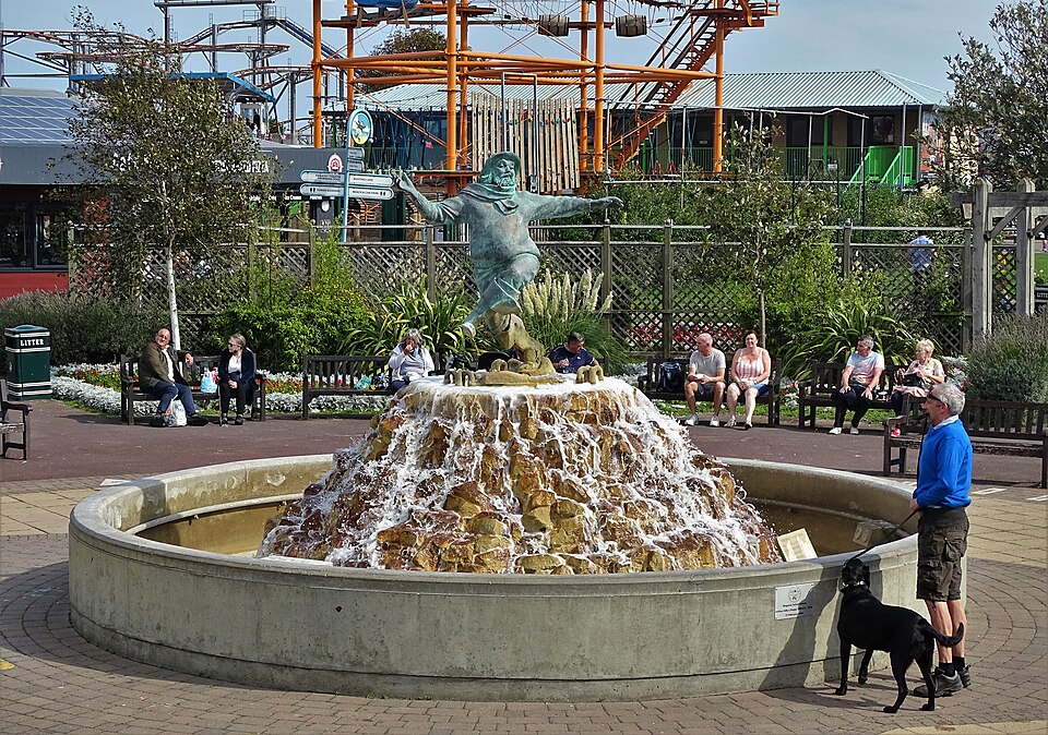 The Jolly Fisherman statue in Skegness standing on top of a fountain, with a man and his dog admiring it on a sunny day.